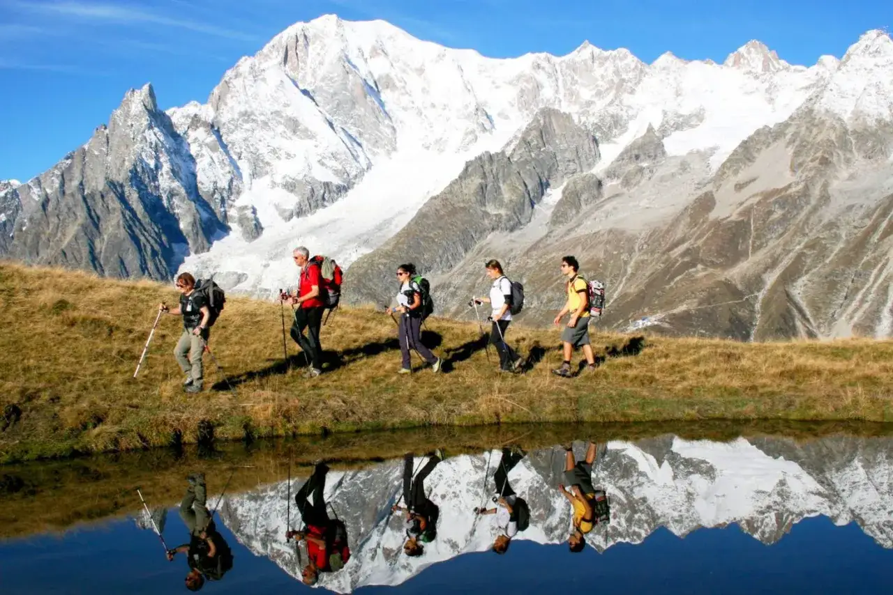 Cinq randonneurs marchent sur un sentier herbeux avec le Mont Blanc enneigé en arrière-plan. La difficulté du Tour du Mont Blanc est évidente dans ce paysage majestueux.
