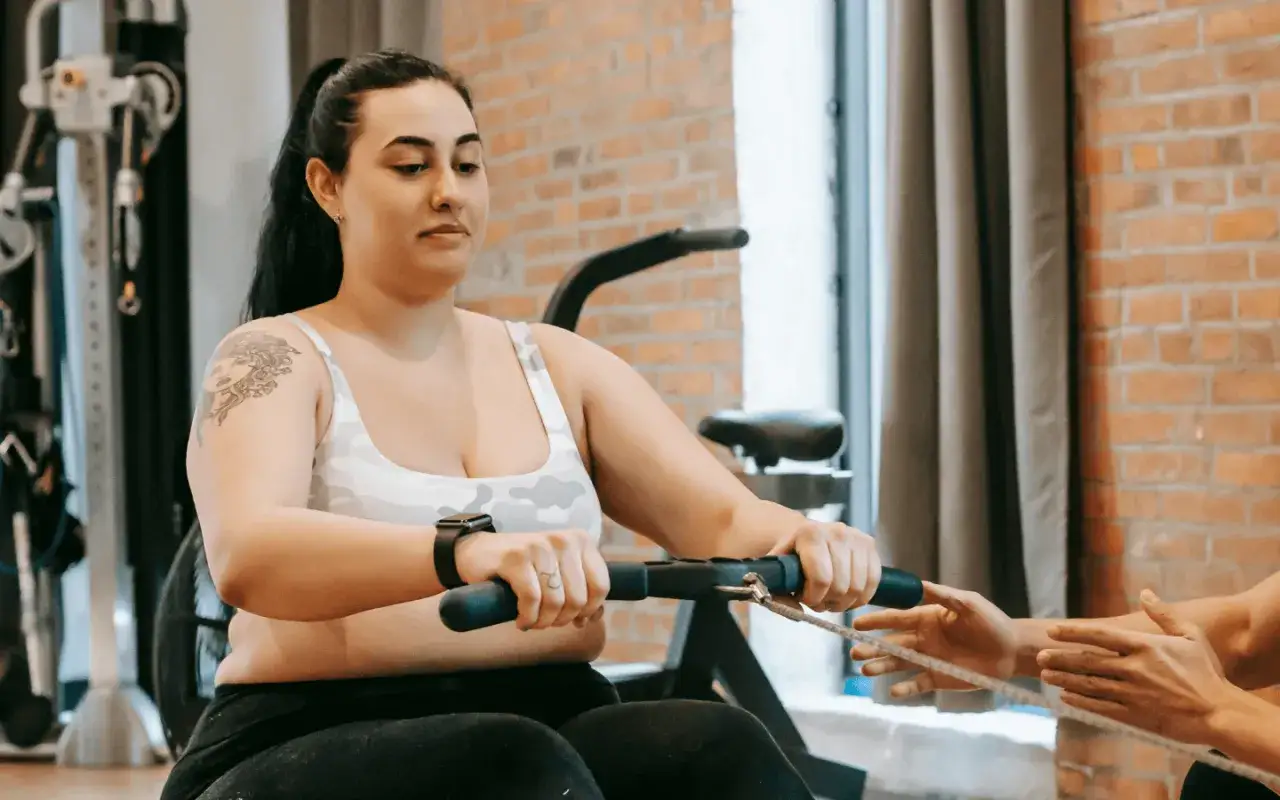 Une femme fait un entraînement rameur, concentrée sur son effort. Une autre personne l'aide.
