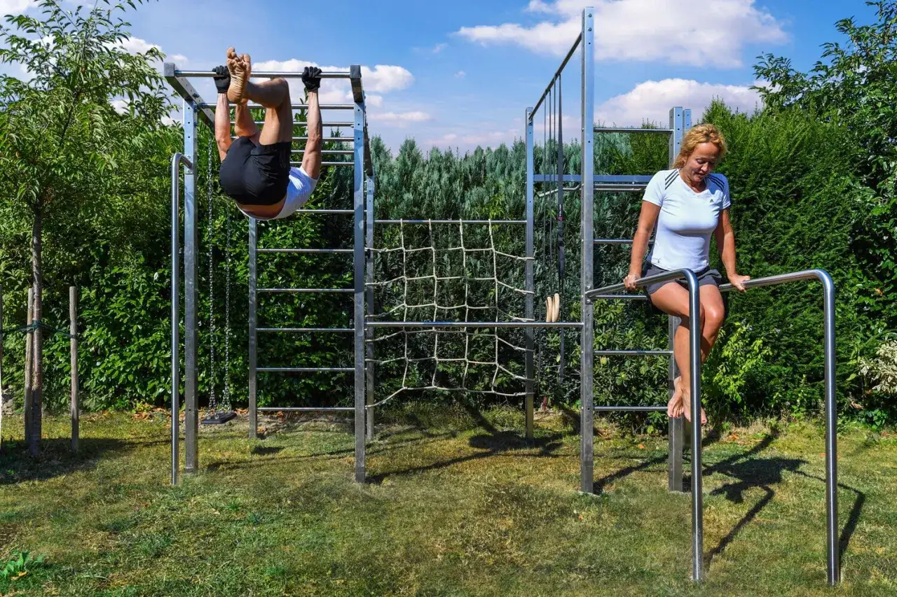 Un homme s'entra&icirc;ne sur une barre fixe, une femme sur des barres parall&egrave;les. Un &eacute;quipement de callisth&eacute;nie programme en plein air.
