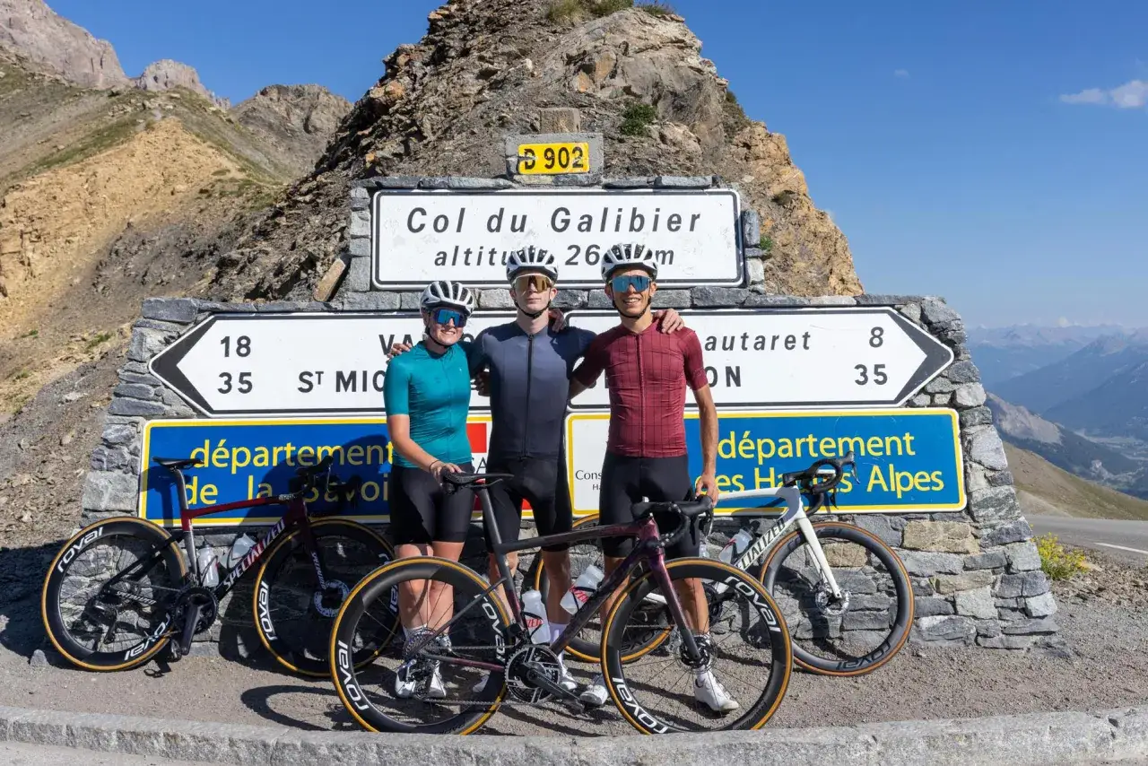 Trois cyclistes posent fi&egrave;rement devant le panneau du Col du Galibier, altitude 2645m, apr&egrave;s une ascension difficile.