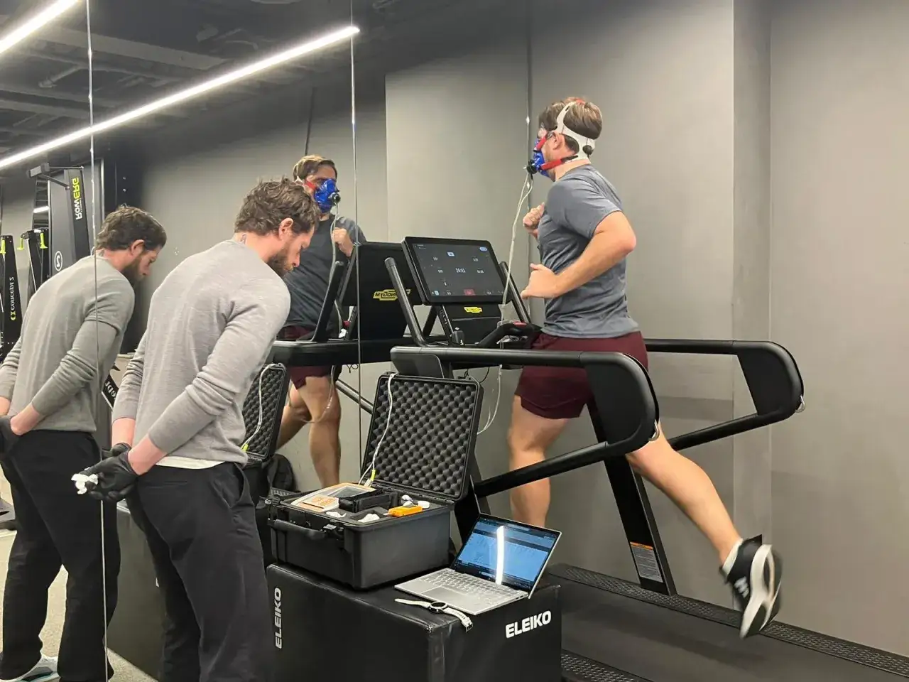 Homme courant sur tapis roulant avec masque pour mesurer le VO2 max. Des techniciens surveillent les données sur un ordinateur portable.