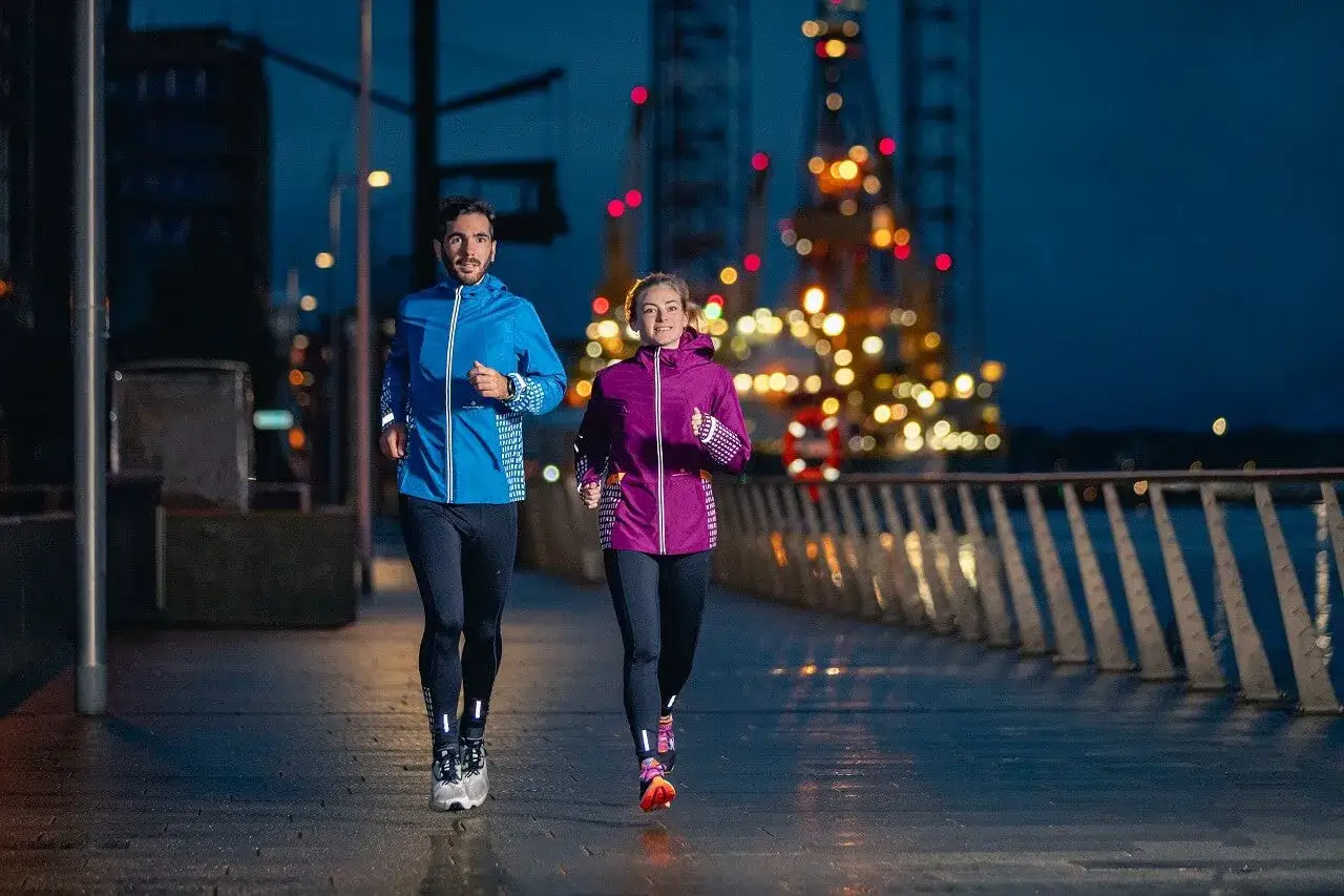Un couple court sur un quai illuminé par des lumières urbaines. Ils profitent de leur séance de sport, que ce soit pour courir le matin ou le soir.