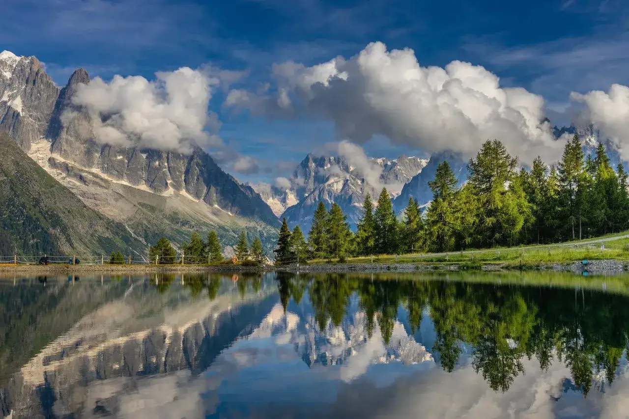 Un lac alpin reflète des montagnes majestueuses et des nuages cotonneux. Parfait pour une randonnée 1 journée.