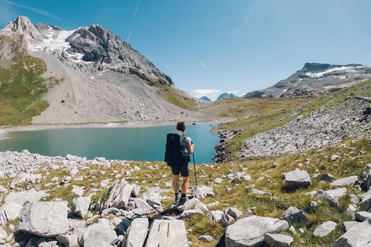 Randonneur contemplant un lac turquoise lors du tour des glaciers de la Vanoise 3 jours. Paysage alpin spectaculaire.
