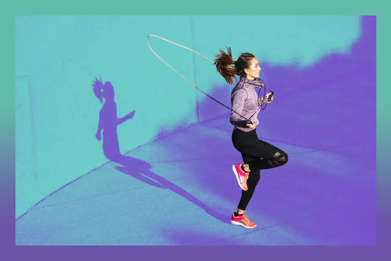 Une femme s'entra&icirc;ne avec une corde &agrave; sauter, profitant du bienfait corde &agrave; sauter pour sa forme physique. Son ombre se projette sur le mur color&eacute;.