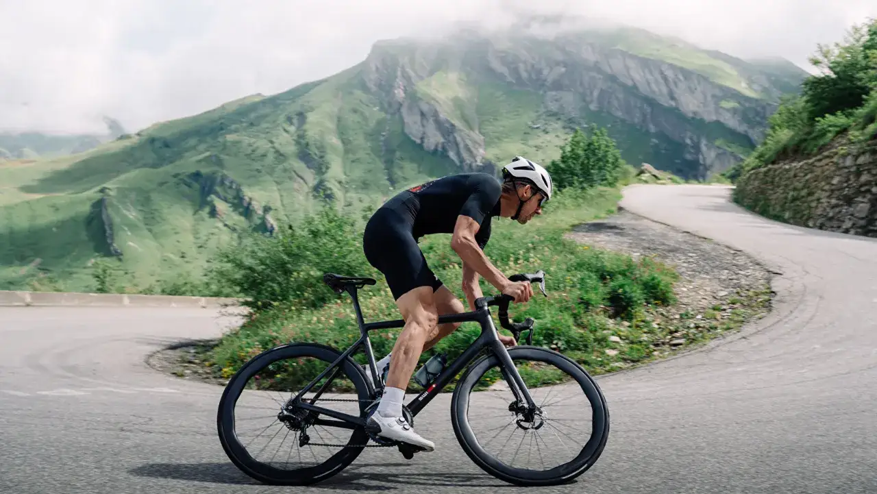 Cycliste en tenue noire gravissant une route sinueuse de montagne, profitant de l'ouverture des cols savoyards.