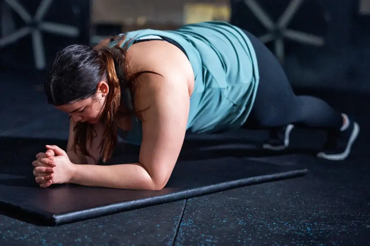 Une femme fait la planche, un excellent sport pour perdre du ventre. Elle est concentrée et déterminée.