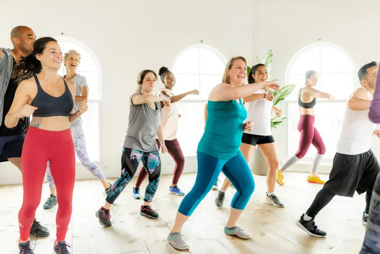 Un groupe de personnes souriantes participe à un cours de zumba pour maigrir, bougeant en rythme dans une salle lumineuse.