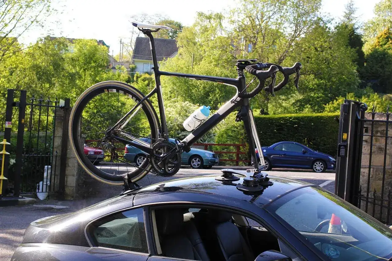 Un v&eacute;lo de course noir est fix&eacute; sur le toit d'une voiture gr&acirc;ce &agrave; un montage porte v&eacute;lo.