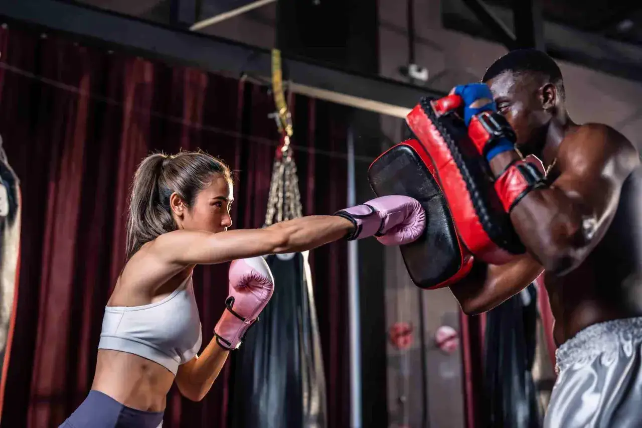 Une boxeuse à l'entraînement, elle frappe un pad tenu par son coach. Quel est le meilleur sport pour se dépasser ? La boxe, sans aucun doute !