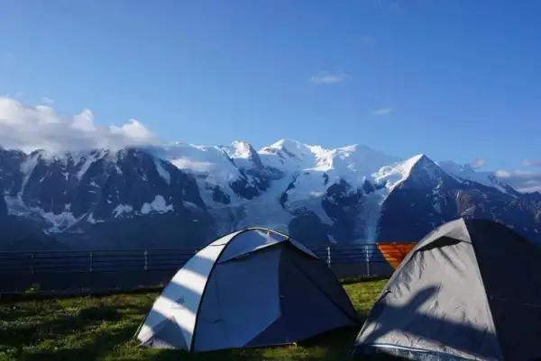 Deux tentes de bivouac aiguilles rouges face à des montagnes enneigées sous un ciel bleu.