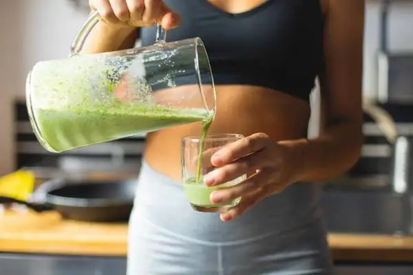 Une femme verse un smoothie vert dans un verre, un geste essentiel pour réussir son challenge 75 Hard.