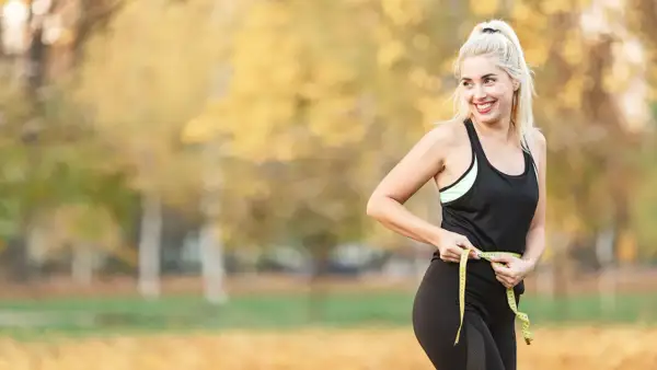 Femme souriante mesurant sa taille avec un mètre ruban, prouvant que courir fait il maigrir.
