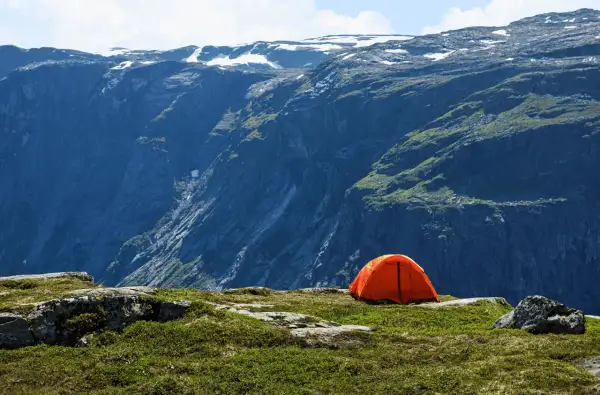 Orange tente sur un plateau rocheux, avec une vue imprenable sur des montagnes escarpées. Un endroit parfait pour un bivouac autorisé.
