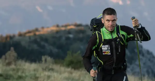 Un homme en tenue de sport, sac à dos et bâtons, progresse sur un trail montagneux au lever du soleil.