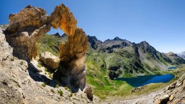 Un arc rocheux spectaculaire domine un paysage de montagne verdoyant avec des lacs bleus, une vue typique du tour du Mercantour.