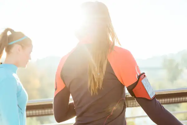 Deux femmes s'entraînent dehors, profitant du soleil. L'une porte un brassard pour son téléphone, prête à courir sous 30 degrés.