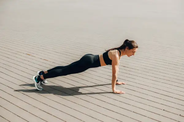 Femme en tenue de sport faisant une planche sur un sol pavé. Elle est concentrée, le corps gainé. Quel est le meilleur sport ? Celui qui vous fait vous sentir ainsi !
