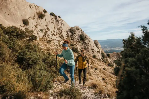 Deux randonneurs font du fast hiking sur un sentier rocailleux, profitant d'un paysage montagneux spectaculaire.