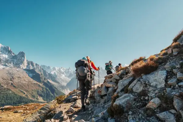 Randonneurs sur un sentier rocheux, le Tour du Mont Blanc difficulté est palpable. Paysage alpin grandiose sous un ciel bleu.