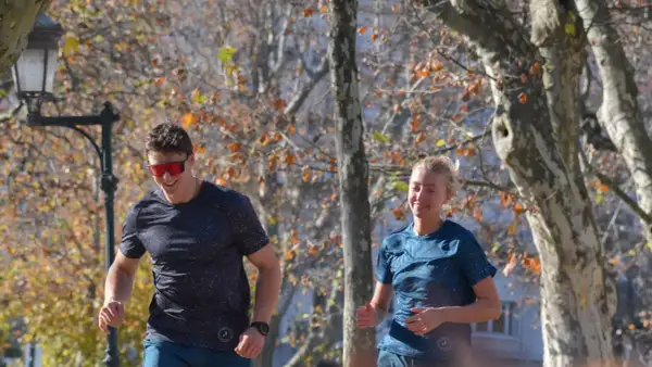 Un homme et une femme souriants courent dans un parc en automne, profitant de leur endurance fondamentale.
