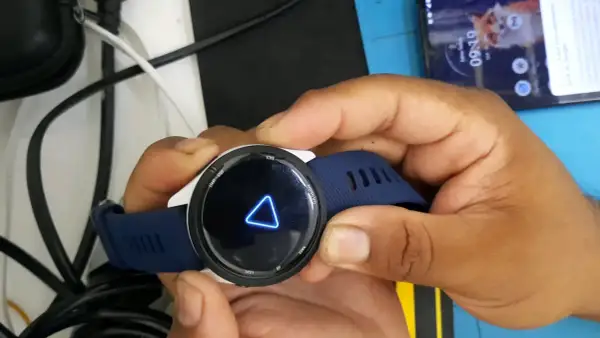 Montre Garmin avec un triangle bleu lumineux sur l'écran. La montre est tenue par des mains.
