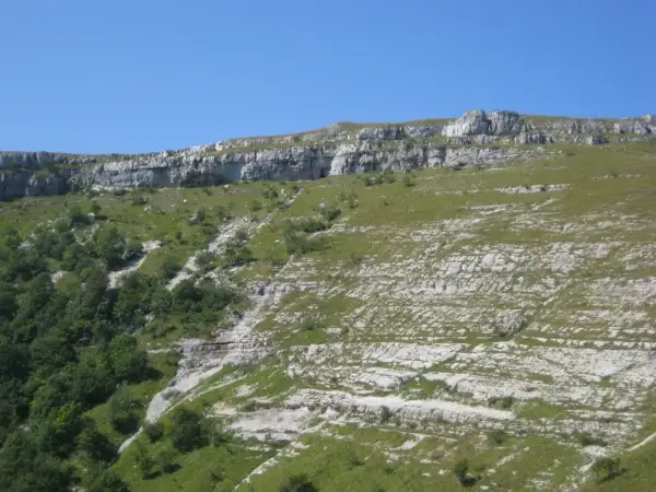 Paysage rocheux et verdoyant du Jura, idéal pour une randonnée boucle 5 jours. Le sentier serpente entre falaises et prairies.