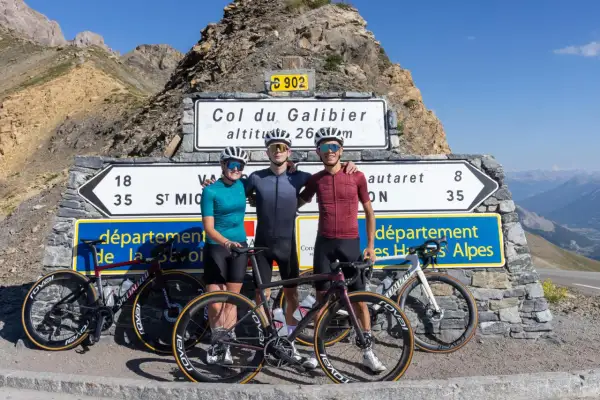 Trois cyclistes posent fièrement devant le panneau du Col du Galibier, altitude 2645m, après une ascension difficile.