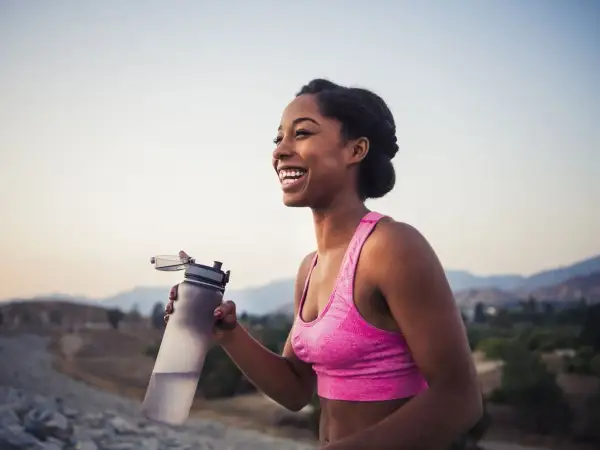 Une femme souriante tient une bouteille d'eau après son entraînement. Le sport est essentiel pour la perte de poids et le bien-être.
