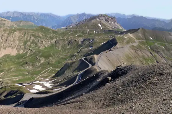 Vue panoramique du col de la Bonette, avec sa route sinueuse traversant des paysages montagneux verdoyants et rocailleux.