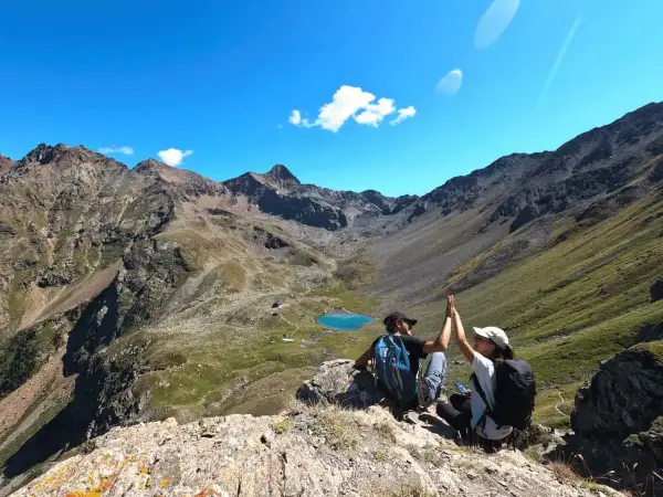 Deux randonneurs célèbrent leur succès au sommet, avec un lac bleu et des montagnes majestueuses en arrière-plan. Une parfaite randonnée à Aoste.