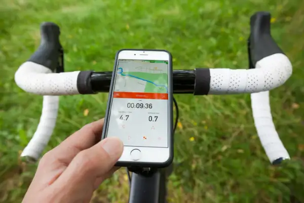 Un cycliste utilise son smartphone avec une application type komoot ou Strava pour suivre sa sortie. La carte et les stats sont visibles.