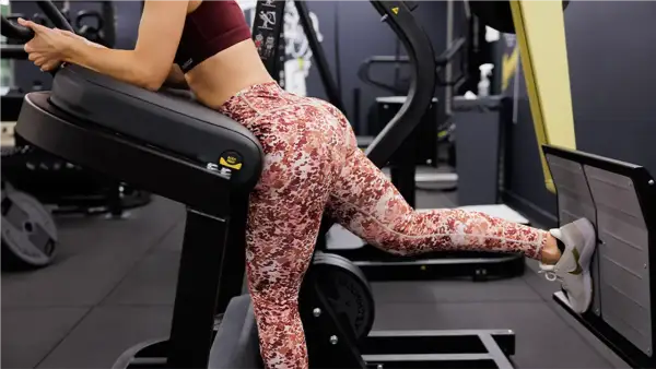 Femme effectuant un exercice fessier sur une machine de musculation, concentrée sur le renforcement de ses muscles.