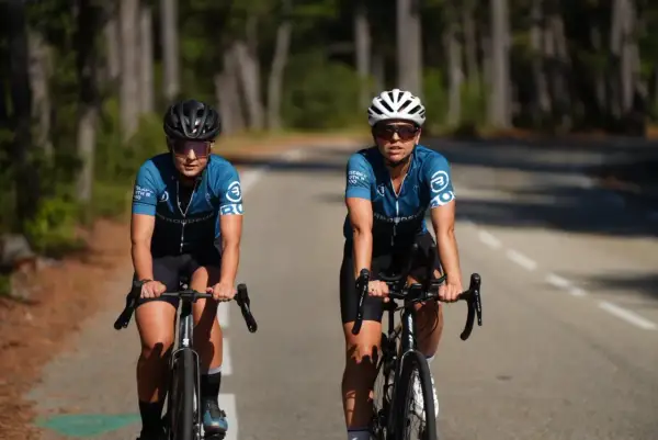 Deux cyclistes en tenue bleue sur la route, prêtes à commencer le vélo de route. Casques et lunettes de soleil pour affronter le soleil.