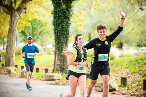Coureurs souriants lors d'une course, un homme agite la main. Idéal pour un plan entraînement semi-marathon débutant.