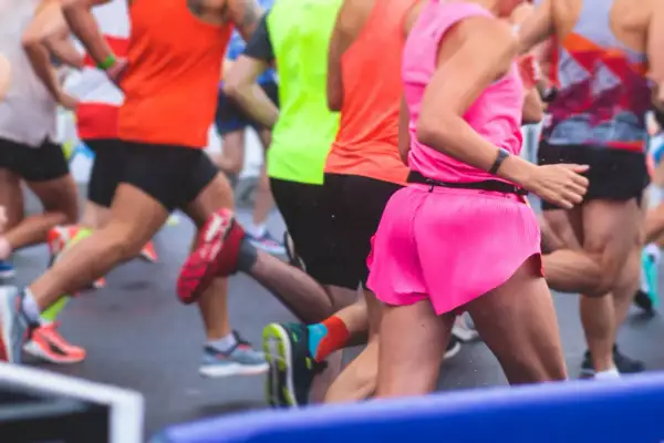 Des coureurs en tenues vives s'élancent sur la piste mouillée. L'un d'eux, en rose vif, semble vivre son premier marathon, déterminé.