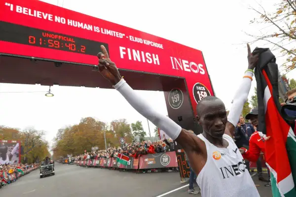 Eliud Kipchoge franchit la ligne d'arrivée, record marathon homme officiellement battu. Il brandit le drapeau kenyan, célébrant son exploit.