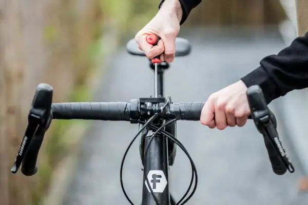 Ajustement du guidon de vélo avec un tournevis. Les mains manipulent la potence pour remonter le guidon vélo.